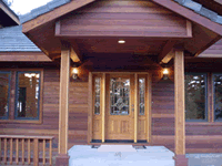 Front entrance of a wooden house with double glass doors, a covered porch, and steps leading up to it.