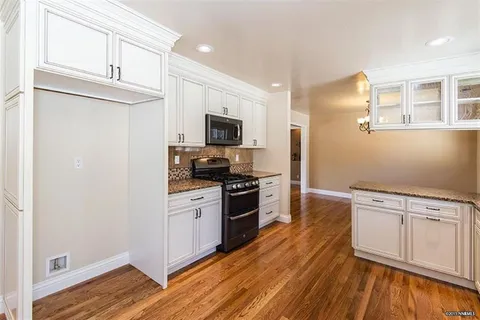 Bright white kitchen with white cabinets, granite countertops, and a black freestanding stove on warm wood flooring.