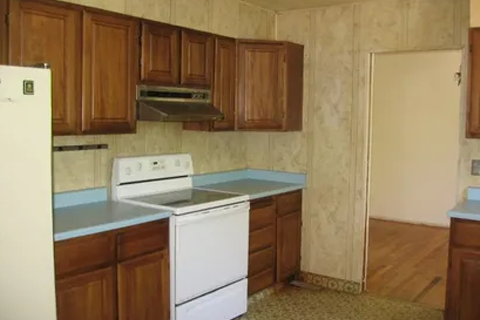 Old-style kitchen with brown wooden cabinets, light blue countertops, and white stove and dishwasher in a compact layout.