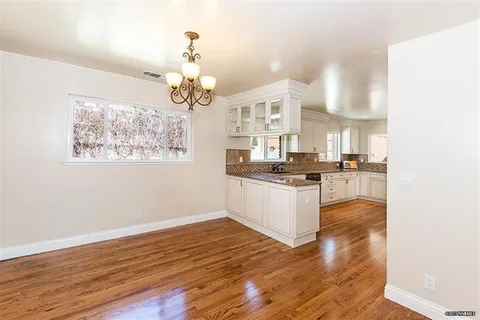 Open-concept living and kitchen area with hardwood floors, white cabinets, and island in the center.