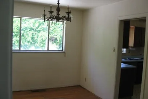 Empty dining area with a chandelier, a large window, and an open doorway to the kitchen.