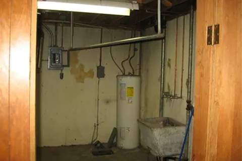 Utility room in a basement with a white water heater, exposed pipes, and a sink.