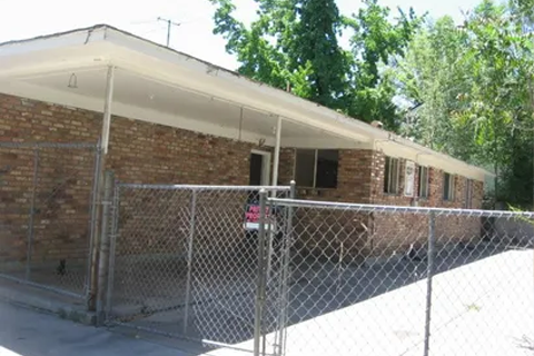 Front view of a low, flat-roofed brick building with a chain-link fence and gate in the foreground.